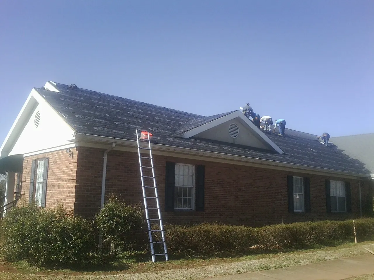 Crew tearing shingles off a brick ranch roof with a ladder set — Metal Roof Repair work by our crew in Rimersburg