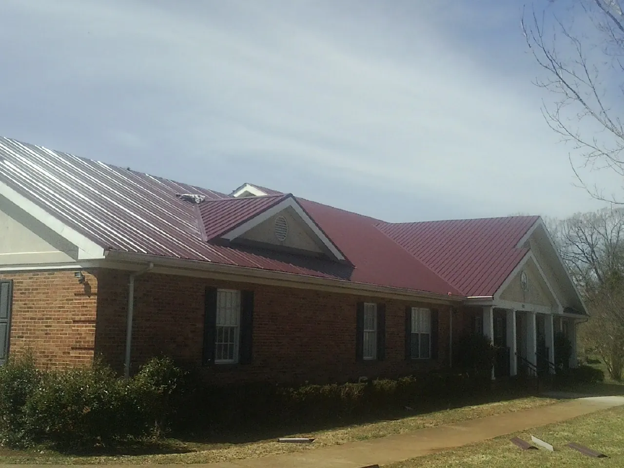 Red metal roof with gabled entries on a long brick building, from a Hail Damage Roof Repair job in Rimersburg
