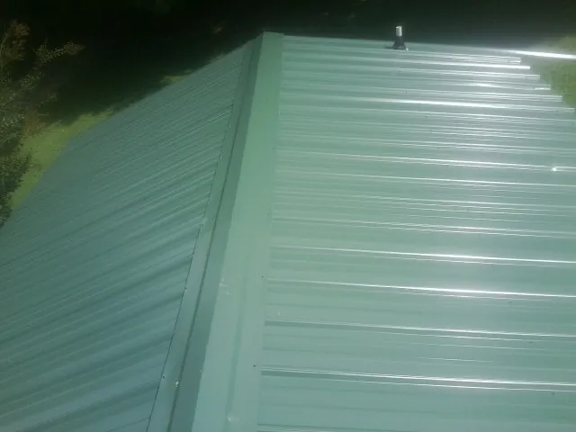 New green metal panels meeting at the ridge of a roof — Flat Roof Repair work by our crew in Rimersburg