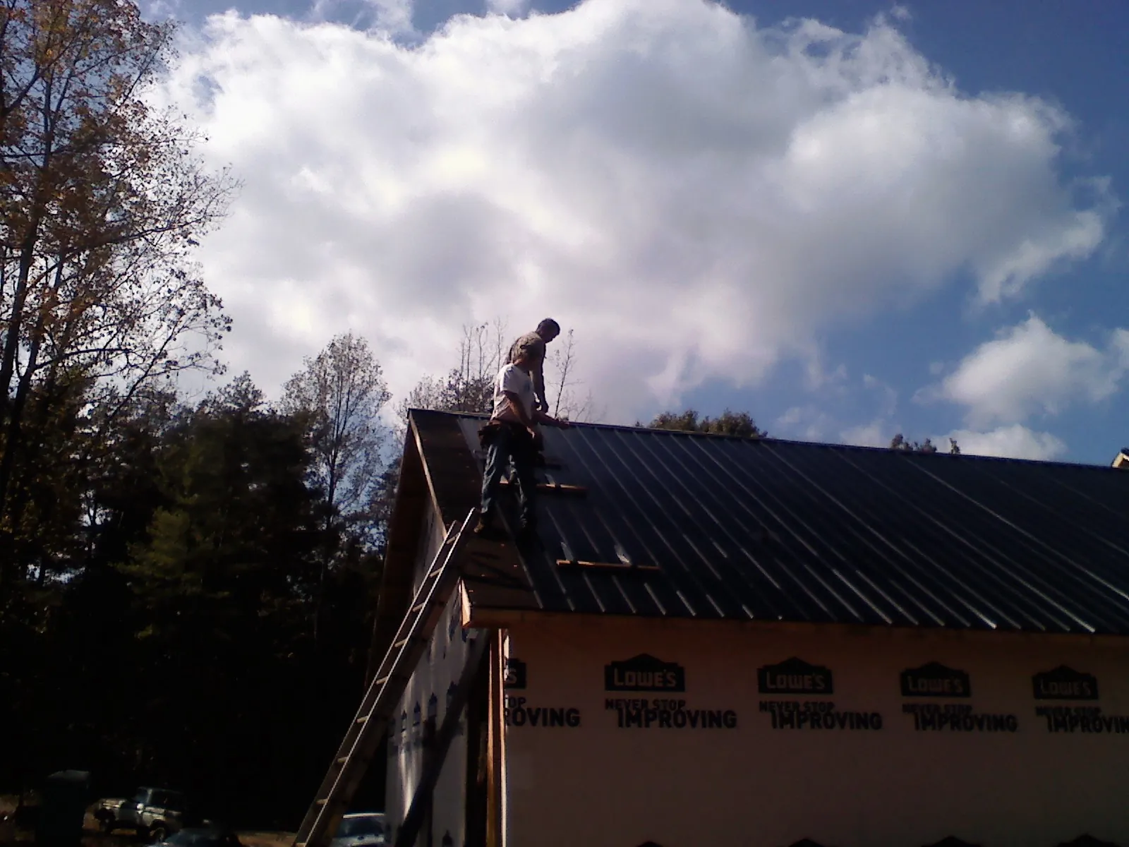 Roofer fastening dark metal panels high against a cloudy sky, from a Roof Inspection job in Rimersburg