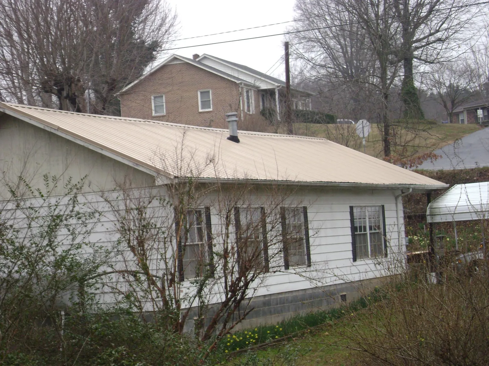 Tan metal roof on a white sided house set into a hillside — Commercial Roofing by Roofing Brothers in Rimersburg